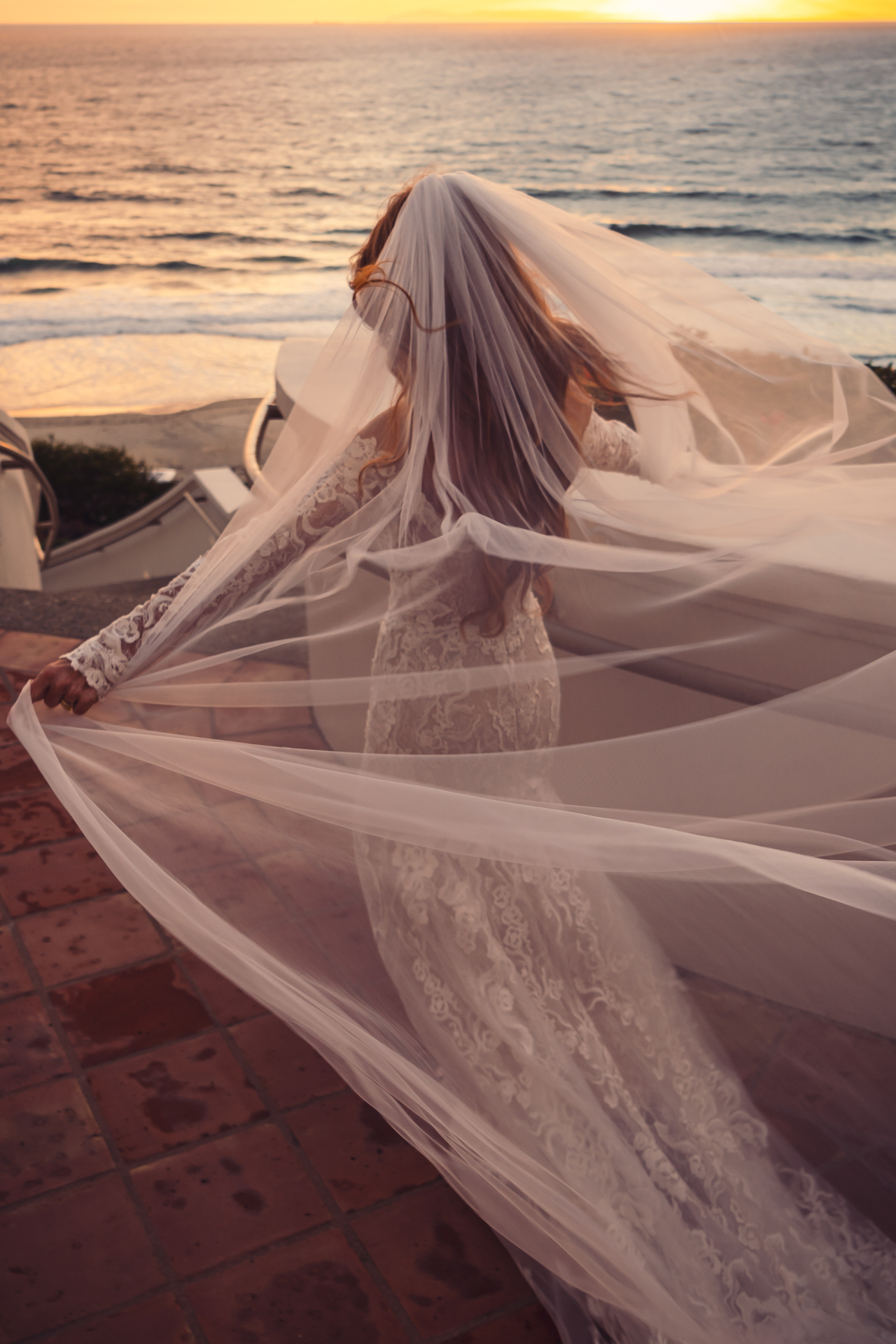 Bride in lace gown with veil at sunset by the ocean