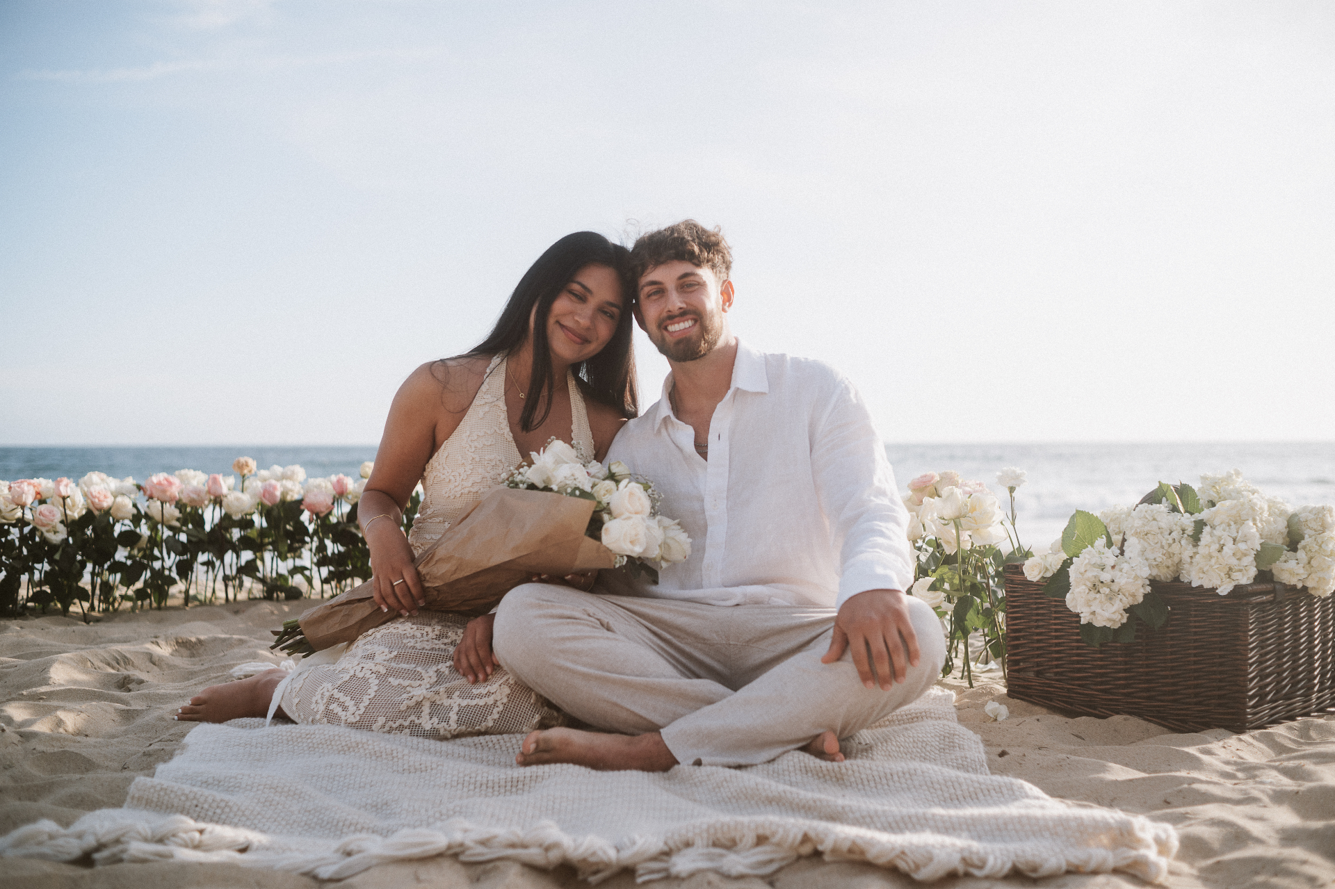 Engaged couple on the beach surrounded by white florals